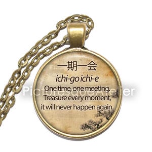 Peut inclure: Un collier en or avec un pendentif rond sur lequel sont inscrits les caractères japonais pour "ichi-go ichi-e" et la traduction anglaise "One time, one meeting. Treasure every moment, it will never happen again."