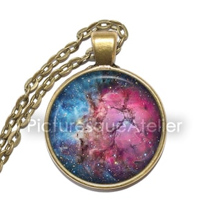 Peut inclure: Un collier en chaîne dorée avec un pendentif rond représentant une nébuleuse colorée. Le pendentif présente une nébuleuse bleu foncé, rose et violette avec une dispersion d'étoiles.