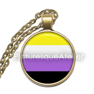 Könnte beinhalten: Halskette mit goldfarbener Kette und rundem Anhänger. Der Anhänger zeigt die Non-Binary-Pride-Flagge in Gelb, Weiß, Lila und Schwarz. Der Text "Picturesque Atelier" ist auf dem Anhänger aufgedruckt.