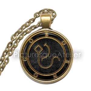 Può includere: Una collana con catena dorata con un ciondolo rotondo nero e oro che presenta un sigillo con le lettere "B.O.N.R." attorno al bordo.