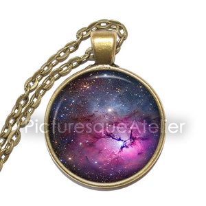 Peut inclure: Un collier en chaîne dorée avec un pendentif rond représentant une nébuleuse colorée. Le pendentif présente une nébuleuse bleu foncé, violette et rose avec une étoile blanche brillante au centre.