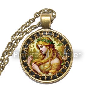 May include: A gold necklace with a round pendant featuring a painting of a woman with long blonde hair wearing a crown of leaves. The pendant is surrounded by a black circle with gold runes.