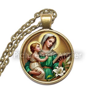 Può includere: Una collana con pendente dorato raffigurante un'immagine religiosa di una donna e un bambino. La donna indossa una veste verde e tiene un libro, con un'aureola intorno alla testa. Il bambino è vestito di bianco. Una catena dorata sospende il pendente.