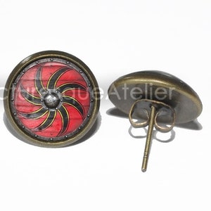 May include: A pair of bronze stud earrings featuring a red and black shield design. The shield has a black and yellow spiral pattern and a silver center.