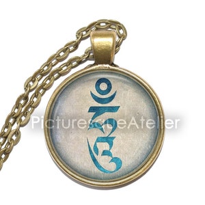 Op de afbeelding: Een gouden ketting met een ronde hanger met een blauw Om-symbool op een witte achtergrond.