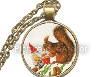 May include: A round glass pendant necklace with a bronze chain features a gnome with a red hat and a squirrel holding a basket of nuts. The pendant has a white background with a snowy scene.