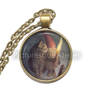 May include: A round glass pendant necklace with a gold chain. The pendant features a whimsical illustration of a gnome holding a lit candle, a cat, and a mouse. The background is a dark blue with a hint of purple.