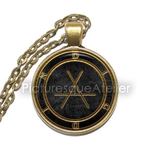 May include: A gold chain necklace with a round pendant featuring a black background and a gold sigil with the letters "D", "I", "G", and "N" around the edge.
