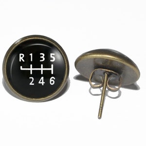 May include: A pair of bronze-colored earrings with a black circular charm featuring a white gear shift pattern with the numbers R135 and 246.