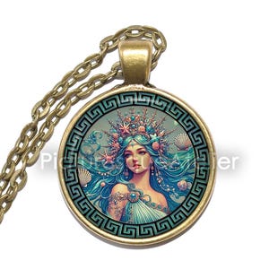 May include: A bronze pendant necklace with a chain. The pendant displays a detailed illustration of a mermaid with blue hair and a crown, framed by a Greek key border. The mermaid wears a turquoise dress.