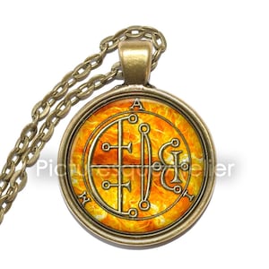 May include: A gold chain necklace with a round pendant featuring a yellow and orange sigil with the letters 'A', 'N', and 'I' on a fiery background.