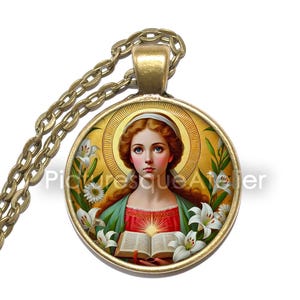 May include: A round pendant necklace with a religious image. The pendant features a portrait of a woman with a halo, surrounded by white lilies. The chain and pendant frame are gold-coloured.