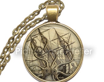 Op de afbeelding: Een gouden ketting met een ronde glazen hanger met een vintage illustratie van een octopus die een zeilschip aanvalt.