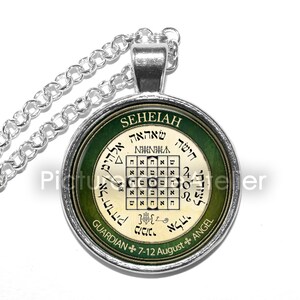 May include: Silver necklace with a round pendant featuring a green and white design. The pendant has the Hebrew word "SEHEIAH" at the top and the text "GUARDIAN 7-12 August ANGEL" at the bottom. The pendant also features a square with Hebrew letters inside.