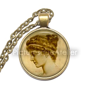 May include: A gold chain necklace with a round pendant featuring a sepia-toned image of a woman's profile. The pendant has a gold rim.