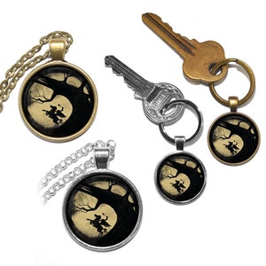 May include: Two silver and bronze necklaces with a round pendant featuring a black silhouette of a witch riding a broomstick in front of a full moon and a tree. The pendant is attached to a silver chain and a bronze chain.
