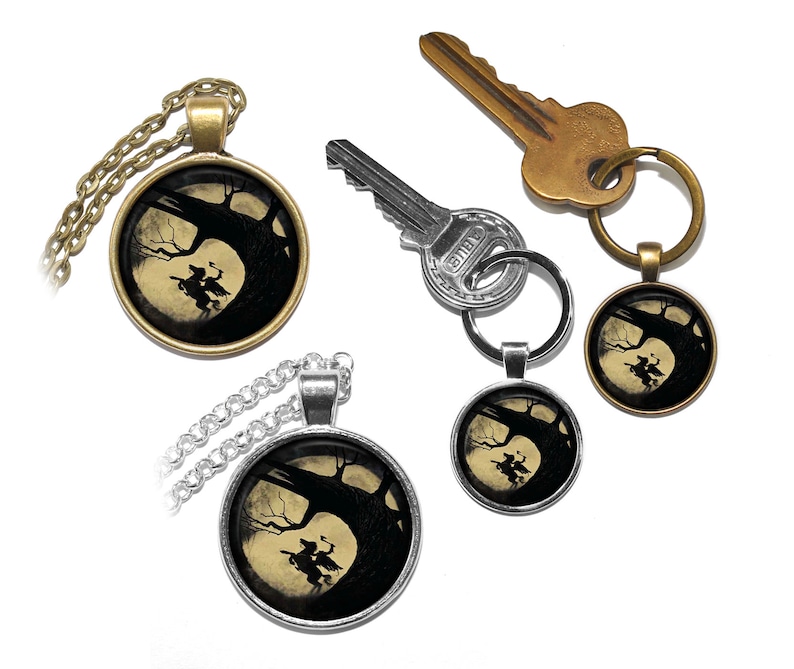 May include: Two silver and bronze necklaces with a round pendant featuring a black silhouette of a witch riding a broomstick in front of a full moon and a tree. The pendant is attached to a silver chain and a bronze chain.