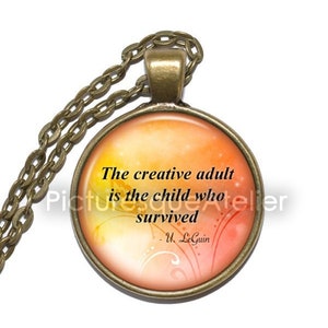 May include: A bronze necklace with a round glass pendant featuring a quote by Ursula K. Le Guin: "The creative adult is the child who survived." The pendant has a watercolour-like background with orange, yellow, and red hues.