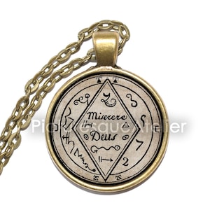 May include: A gold chain necklace with a round pendant featuring a black and white image of a sigil with the text "Misere Deus" and other symbols.