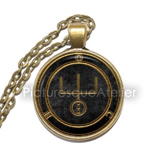 May include: A gold chain necklace with a round pendant featuring a black background and a gold sigil. The sigil is a stylized symbol with three vertical lines and a circle with three dots.