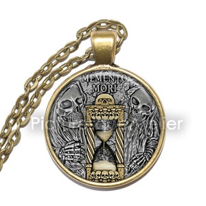 May include: A gold necklace with a round pendant featuring two skeletons flanking an hourglass with the inscription "Memento Mori".