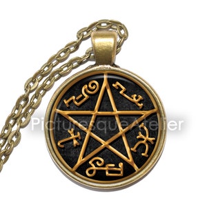 May include: A gold necklace with a round pendant featuring a black background and a gold pentagram with symbols around it.