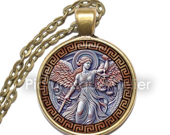 Puede incluir: Un collar de oro con un colgante redondo que presenta una imagen detallada de una figura alada sosteniendo una balanza y una espada. El colgante está rodeado por un borde decorativo de un patrón de llave griega repetido.