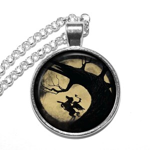 May include: A silver necklace with a round pendant featuring a black silhouette of a rider on horseback against a full moon and a dark tree. The pendant is set in a silver bezel.