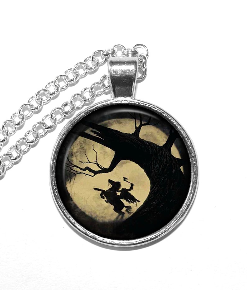 May include: A silver necklace with a round pendant featuring a black silhouette of a rider on horseback against a full moon and a dark tree. The pendant is set in a silver bezel.