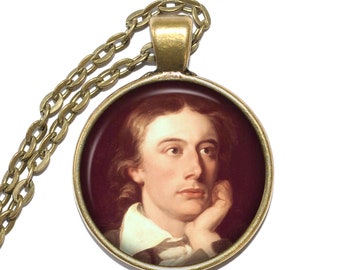 May include: A gold chain necklace with a round pendant featuring a portrait of a man with brown hair and a white collar. The portrait is set against a dark red background.