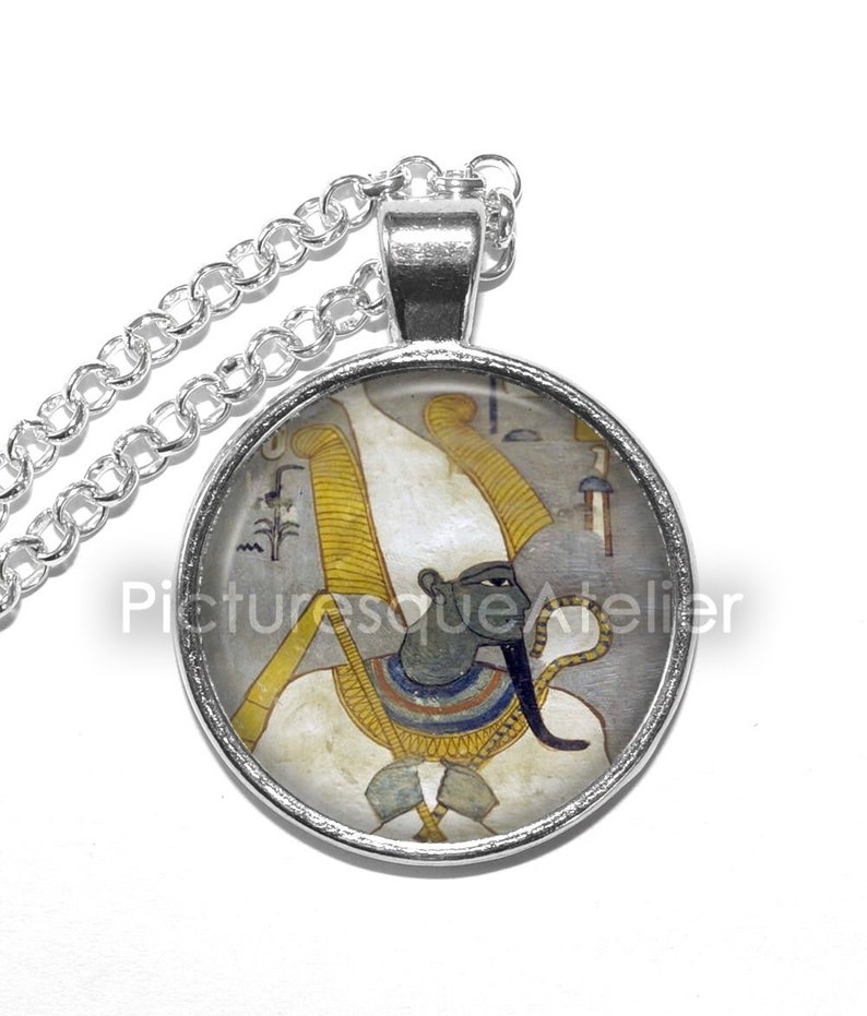 May include: Silver necklace with a round glass pendant featuring a colorful image of an Egyptian god with a white headdress and a blue face.