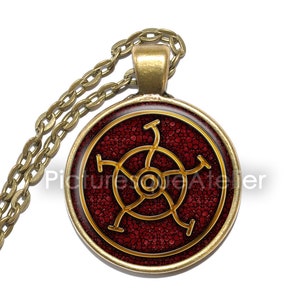 May include: A gold chain necklace with a round pendant featuring a red and gold symbol with a circular design. The symbol is set against a red background with a textured pattern.
