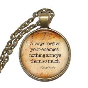 Op de afbeelding: Een ronde glazen hangerketting met een bronzen ketting. De hanger heeft een vintage-achtige achtergrond met de quote "Vergeef je vijanden altijd; niets ergert ze zo - Oscar Wilde".
