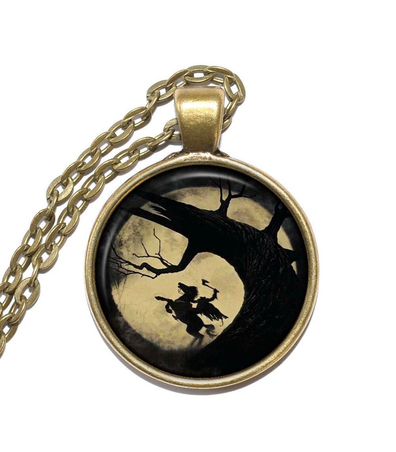 May include: A gold chain necklace with a round pendant featuring a black silhouette of a rider on horseback against a full moon and a dark tree.