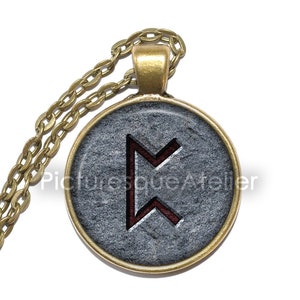 Puede incluir: Un collar de cadena dorada con un colgante redondo que presenta una piedra gris con un símbolo de runa roja. La runa es el símbolo de Elder Futhark para 'Ehwaz', que representa la asociación, el viaje y el movimiento.