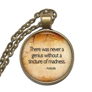 Könnte beinhalten: Eine bronzene Halskette mit einem runden Glasanhänger, auf dem ein Zitat von Aristoteles steht: "Es gab noch nie ein Genie ohne einen Hauch von Wahnsinn." Das Zitat ist auf einem Hintergrund im Vintage-Look gedruckt.
