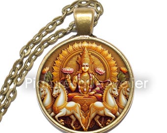 May include: A round pendant necklace with a detailed illustration of a deity seated on a throne, surrounded by a golden sunburst and horses. The pendant is attached to a bronze-colored chain.