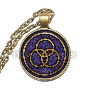 Könnte beinhalten: Eine goldene Kettenkette mit einem runden Anhänger mit violettem Hintergrund und einem goldenen, ineinandergreifenden Kreisdesign.
