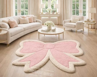 May include: A large, pink bow-shaped rug with a cream-colored border sits on a light wood floor. The rug is the focal point of a bright, airy living room with white furniture and gold accents. The rug's design adds a touch of whimsy to the space.
