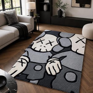 Puede incluir: Una alfombra rectangular con un dise&ntilde;o de personaje de dibujos animados estilizado en tonos gris, blanco y negro. El personaje tiene una cabeza similar a una calavera con ojos en forma de X, manos enguantadas y una superficie texturizada.