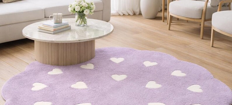 May include: A lavender area rug with a scalloped edge and a repeating pattern of white hearts. The rug has a soft, textured pile and is shaped like a cloud, featuring multiple white heart shapes distributed across the purple surface.