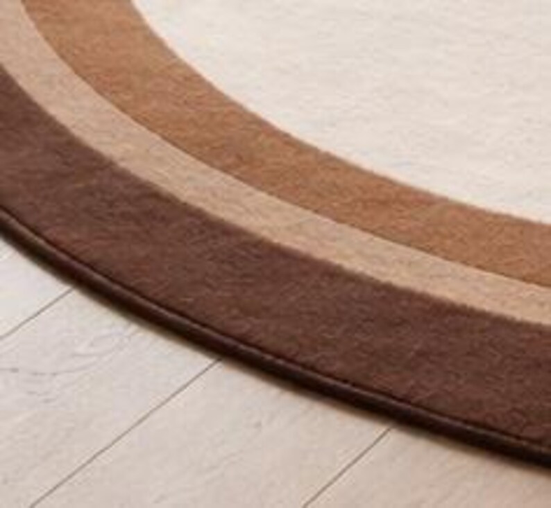 May include: Close-up of a section of a round rug with a rainbow design. The rug features bands of color in shades of brown, beige, and cream. The rug is placed on a light-colored wooden floor.