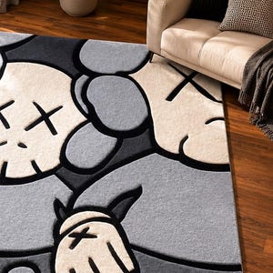 Puede incluir: Una alfombra rectangular con un patr&oacute;n gr&aacute;fico repetitivo de personajes de dibujos animados estilizados con ojos en forma de X. El dise&ntilde;o utiliza una paleta de colores crema, gris claro y gris oscuro, con contornos negros gruesos.