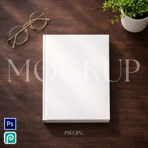 May include: A white book with the word "MOCKUP" faintly visible, along with gold-rimmed glasses and a small potted plant on a dark wood surface. The image also includes the text "PSD/JPG".