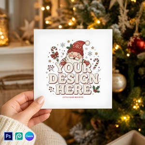 Puede incluir: Una tarjeta cuadrada blanca con un dibujo de Santa Claus con gorro rojo, rodeado de bastones de caramelo, acebo y copos de nieve. El texto YOUR DESIGN HERE aparece en letras grandes, con LITTLE BASH MOCKUPS en letra pequeña.