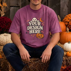 May include: A mauve short-sleeve t-shirt featuring a graphic print with a ghost, a crescent moon, stars, a spider, and a jack-o'-lantern. The text "YOUR DESIGN HERE" is printed in the center in a bold, cream-colored, stylized font.