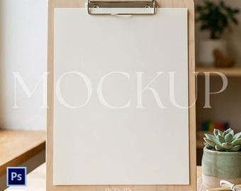 May include: A wooden clipboard with a silver clip holding a blank white paper. The word "MOCKUP" is printed in large, light letters across the paper. A small wooden stand supports the clipboard. The image includes a small succulent in a green pot and a bundle of crayons.