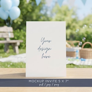 May include: A white invitation card with the text "Your design here" in a cursive font. The card is displayed on a wooden table, with a blurred outdoor background featuring balloons and a picnic setting. The card measures 5 x 7 inches.