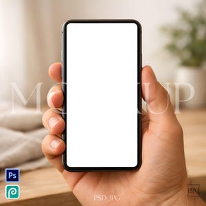 May include: A black smartphone with a blank white screen is held in a person's hand. The phone has a black border and a clean, modern design. The background is blurred, with the word "MOCK UP" faintly visible.
