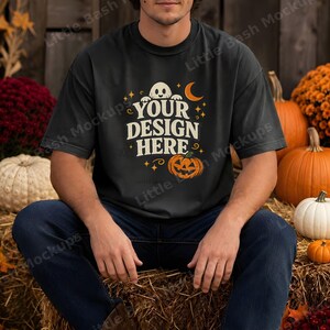 May include: A black short-sleeve t-shirt featuring a graphic print with the text "YOUR DESIGN HERE" in a cream-colored font. The design includes a small white ghost, a crescent moon, stars, and an orange jack-o'-lantern pumpkin illustration.